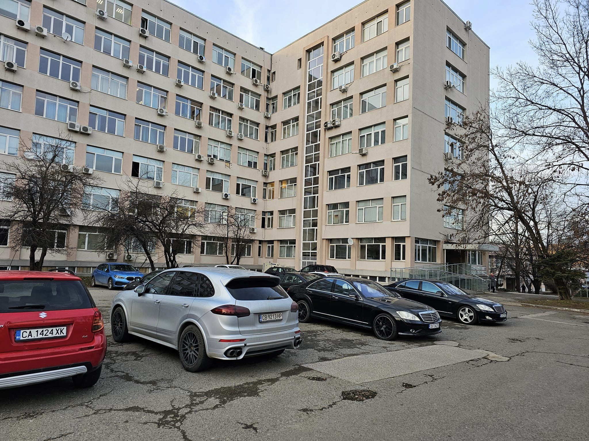 Голям брой луксозни автомобили на паркинга пред сграда в която